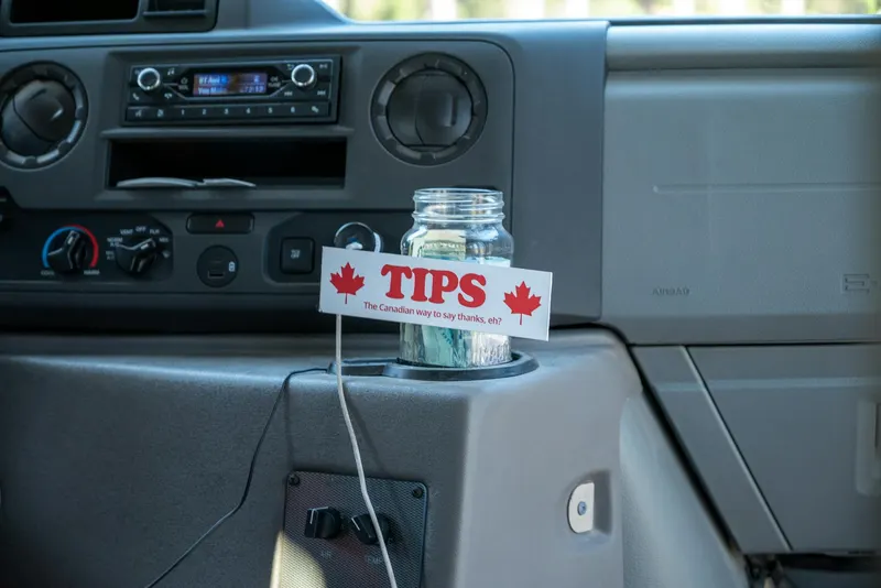 A tip jar labeled 'The Canadian way to say thanks' inside a vehicle's dashboard.